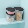 Three clear plastic food storage containers with dark gray lids are stacked on a light blue shelf against a light blue wall. Produktbild-Vorschau