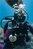A diver is underwater holding a GoPro camera in a protective housing. Voir les images du produit