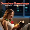 A woman is reading a book in a dimly lit room, illuminated by a rose-shaped lamp worn around her neck. Produktbild-Vorschau