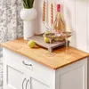 A close-up view of a white kitchen cart with a wooden countertop, decorated with a bottle of wine, two glasses, two lemons, a vase with greenery, and a candelabra with two candles. Produktbild-Vorschau