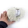 A hand is holding a skein of cream-colored cord on a white background. Podgląd zdjęcia produktu