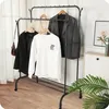 A clothing rack with various garments hanging on it, placed in a room with wooden flooring and a window with curtains in the background. Anteprima dell’immagine prodotto