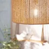 A close-up shot of a lampshade made of woven jute material, with a light bulb glowing inside. Náhľad obrázku produktu