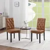 Two brown faux leather dining chairs with tufted backs are placed in a well-lit room with a large window overlooking a garden. Produktbild-Vorschau