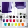 A collage of various colored flower pots with saucers, displayed in a studio-like setting with a blurred background of a modern interior. Produktbild-Vorschau
