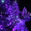 Christmas trees decorated with purple and green lights in the snow at night. Produktbild-Vorschau