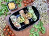 A close-up overhead shot of fresh spring rolls arranged on a black platter, with a small dish of dipping sauce and scattered cherry tomatoes and sprouts around the platter. Produktbild-Vorschau