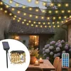 A string of warm white LED lights is draped over a courtyard setting, illuminating a table with candles and flowers. Voir les images du produit