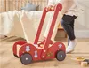 A child is pushing a red wooden walker with animal decorations in a room. Produktbild-Vorschau