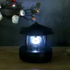 A black solar-powered lighthouse lamp with a bright LED light is displayed on a wooden surface, with a decorative branch with flowers in the background. Anteprima dell’immagine prodotto