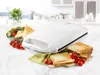 A white sandwich maker is displayed on a kitchen counter with sandwiches and cherry tomatoes. Produktbild-Vorschau