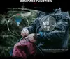 A person in an outdoor setting is shown interacting with a smartwatch that displays compass and time functions. Produktbild-Vorschau