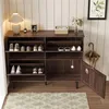 A dark wood shoe cabinet with multiple shelves and flip-down doors, displaying various shoes. An umbrella and a lamp are also visible. Produktbild-Vorschau
