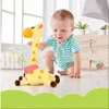 Gelbes Plüsch-Giraffenspielzeug mit orangefarbenen Flecken und einem rosa Tupfenschal, neben einem Baby, das auf einem hellen Boden krabbelt Podgląd zdjęcia produktu