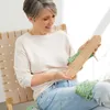 A woman sits in a chair, holding a knitting tool and yarn. Produktbild-Vorschau