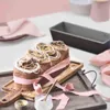 A decorated loaf of bread with icing and nuts, presented on a wooden board with pink ribbon and a small jar of cream. Anteprima dell’immagine prodotto