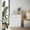 A white dresser with wooden top next to a bed with a wooden headboard, in a room with a large plant and a window. Voir les images du produit
