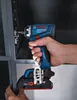 A hand holding a Bosch cordless drill and using it to screw a hinge onto a metal frame. Voir les images du produit