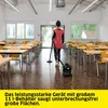 A person is vacuuming a large room with many tables and chairs. Voir les images du produit