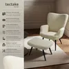 A cream-colored armchair and ottoman set with black legs, displayed on a light-colored rug in a room with wooden flooring and decorative wall molding. Náhled obrázku produktu