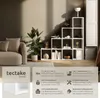 A modern living room scene featuring a white modular bookshelf filled with decorative items and books, next to a beige sofa and a potted plant. Produktbild-Vorschau