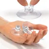 A hand holding several clear suction cups with a slot for cables, with another suction cup being held by fingers above. Produktbild-Vorschau