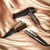 Three black hair styling tools (a hairdryer and two straighteners) are arranged on a draped gold satin fabric. Anteprima dell’immagine prodotto