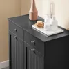 A close-up view of the top and side of a black bathroom cabinet with two drawers and two doors. On top of the cabinet, there is a white tray with several white bottles and a wooden brush. A tall, light brown vase is also on the cabinet. Podgląd zdjęcia produktu