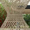 A close-up view of a woven rattan side table in an outdoor setting with greenery in the background. Produktbild-Vorschau