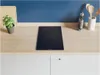 A modern kitchen countertop with a black induction hob, a potted plant, and kitchen utensils. Voir les images du produit