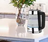 A glass electric kettle sits on a white countertop next to a vase of greenery. Náhled obrázku produktu