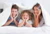 A family is lying in bed under a duvet. Produktbild-Vorschau