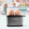 A close-up shot of an anthracite GOURMETmaxx egg cooker with two eggs inside, with a hand in the background reaching for an egg in an egg cup. Náhled obrázku produktu