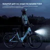 A woman with a bicycle at night, with the bike's headlight on. Produktbild-Vorschau
