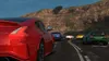 A line of sports cars driving on a winding road with a mountainous landscape in the background. Produktbild-Vorschau