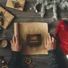 A flat lay of Christmas gifts and a Santa hat on a wooden table, with hands unrolling a scroll of paper. Produktbild-Vorschau