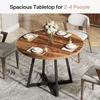 A round wooden dining table with black metal legs, set with placemats, plates, cutlery, and glasses, with a vase of flowers in the center. Chairs are placed around the table. Podgląd zdjęcia produktu