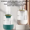 Two humidifiers are shown, one in the foreground and one slightly behind and to the right. The foreground humidifier is teal and white, while the background one is white and gray. Both are emitting mist. Produktbild-Vorschau