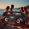A portable speaker is on a beach with people in the background. Produktbild-Vorschau