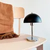 A black and silver table lamp is placed on a wooden chair next to a brown blanket. Produktbild-Vorschau