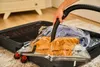 A person is using a vacuum cleaner to suck air out of a vacuum storage bag filled with clothes inside an open suitcase. Náhled obrázku produktu