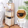 A person is shown interacting with a bamboo laundry basket with three storage bins, highlighting its wheels. Anteprima dell’immagine prodotto