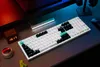 A gaming setup with a white mechanical keyboard, a digital clock, and headphones. Voir les images du produit