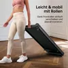 A woman is holding a folded walking pad, demonstrating its portability. The background is a room with wooden flooring and white walls. Produktbild-Vorschau