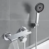 A modern bathroom faucet with a waterfall spout and a handheld showerhead mounted on a tiled wall. Produktbild-Vorschau