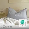 A pillow on a bed with a white duvet and a small vase with a flower on a nightstand. Produktbild-Vorschau
