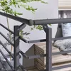A close-up view of a modern gray metal railing system on a balcony, with a potted plant and wooden seating in the background. Produktbild-Vorschau