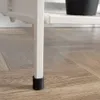 Close-up of the leg of a white metal shelf unit with a black foot cap, resting on a wooden floor. Voir les images du produit