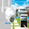 A white outdoor security camera is mounted on a wall, with a smartphone displaying the camera's feed in the foreground. The background shows a house and a swimming pool. Voir les images du produit