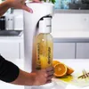 A person is using a Drinkmate carbonation machine to make sparkling water with orange juice. Podgląd zdjęcia produktu